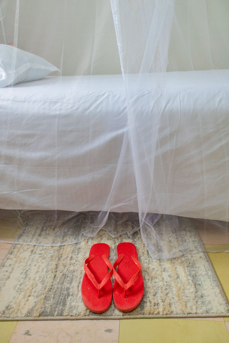 Red slippers on a rug beside a made bed